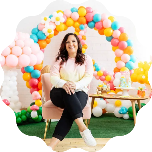 Jenny Porter seated under a rainbow balloon arch